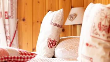 Una cama con ropa de cama blanca y almohadas decorativas, incluyendo una con diseño de corazón, en una habitación con paneles de madera.
