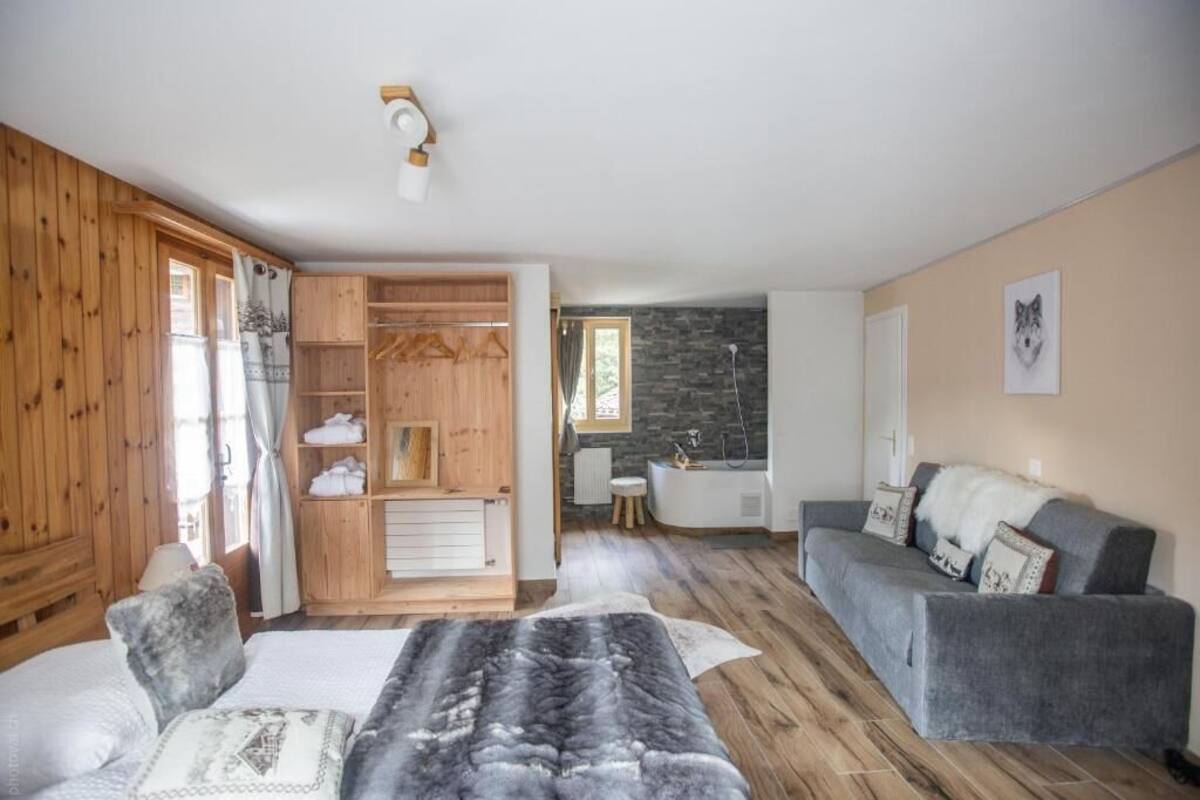 A cozy room with a wooden wardrobe, a grey sofa, and a bed with a patterned blanket.