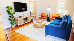 A modern living room with a blue sofa, wooden flooring, a flat-screen TV, and a large plant.