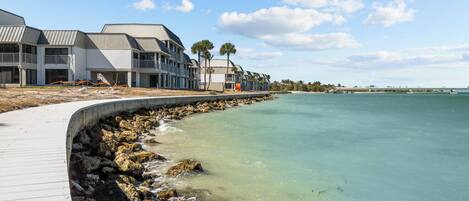 A coastal hotel with a wooden boardwalk leading to the beach, featuring multiple-story buildings with balconies.