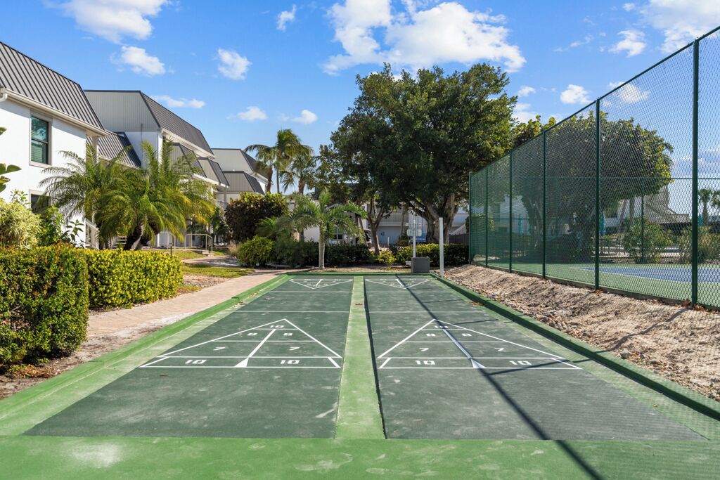 Een groene jeu-de-boulesbaan met een omheining van netten en palmbomen op de achtergrond.