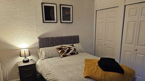 Et soveværelse med en seng, et natbord med lampe, to billeder i rammer på væggen og et garderobeskab.