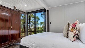 Une chambre avec un grand lit, une armoire et une vue sur les arbres, visible à travers une porte vitrée.