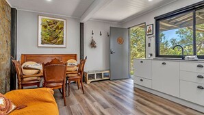 Une cuisine moderne avec un plancher en bois, un coin repas avec une table et des chaises en bois, et une grande fenêtre donnant sur la forêt.