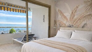 Ein Schlafzimmer mit einem großen Bett, einem Balkon mit Meerblick und einem Wandbild im tropischen Stil.