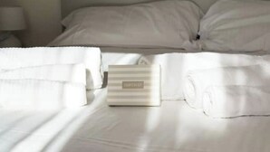 A neatly made bed with white linens, a folded towel, and a small box labeled "COLLECTION 1". - Pittulongu Horizon - Where Blue Meets Relaxation (Olbia)