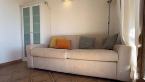 A beige sofa with cushions, a cabinet with glass doors, and a floor lamp in a room with tiled flooring. - Pittulongu Horizon - Where Blue Meets Relaxation (Olbia)