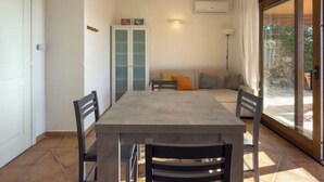 A dining area with a table and chairs, a cabinet, a sofa with cushions, and a sliding glass door leading to an outdoor area. - Pittulongu Horizon - Where Blue Meets Relaxation (Olbia)