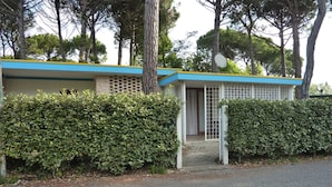 Un edificio pequeño de una sola planta con fachada azul y blanca, un porche cubierto y un seto cuidado.