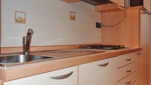 Una cocina con un lavamanos de acero inoxidable, un microondas, armarios de madera y salpicadero de azulejos.