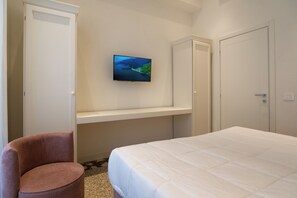 Ein Schlafzimmer mit einem Bett, einem an der Wand befestigten Fernseher, einem Sessel und einem Kleiderschrank.