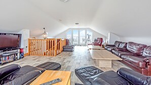 Ett rymligt vardagsrum med en stor TV, lädersoffor, ett soffbord i trä och en balkong med utsikt.