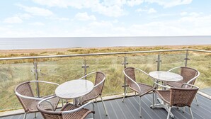 En balkong med flätade stolar och ett glasbord med utsikt över en strand.