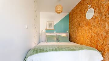 Una cama con colcha verde y blanca, un espejo montado en la pared y una obra de arte enmarcada sobre la cama.
