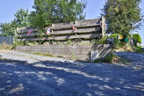 A wooden sign with the text 'LES JARDINS DE LÉCUME' and two flags, one red and one blue, on a gravel path.