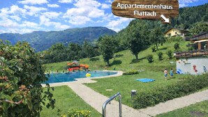 A pool area with a wooden sign indicating 'Apartmentenhaus Flattach'. - Appartementhaus Flattach (Flattach)