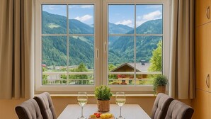 A dining area with a table and chairs, a view of mountains, and a window with curtains. - Appartementhaus Flattach (Flattach)