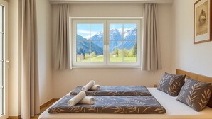 A bedroom with a wooden bed, a window with a mountain view, and a wooden dresser. - Appartementhaus Flattach (Flattach)