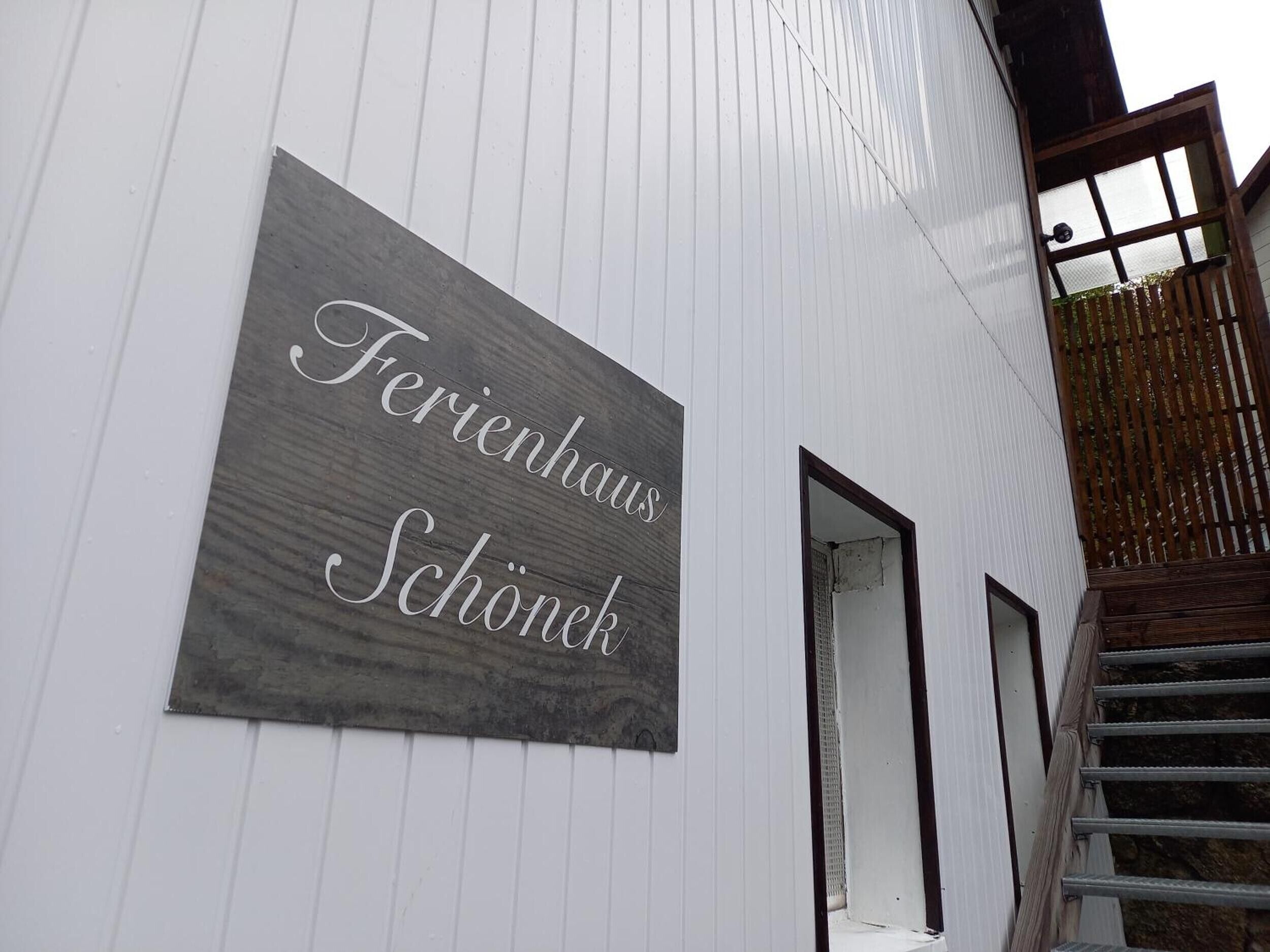 Ein Schild an einem weißen Gebäude mit dem Schriftzug 'Ferienhaus Schönek'.
