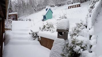 Schnee bedecktes Freigelände mit Holzzaun, kleiner blauer Schuppen und Vogelhaus aus Stein.