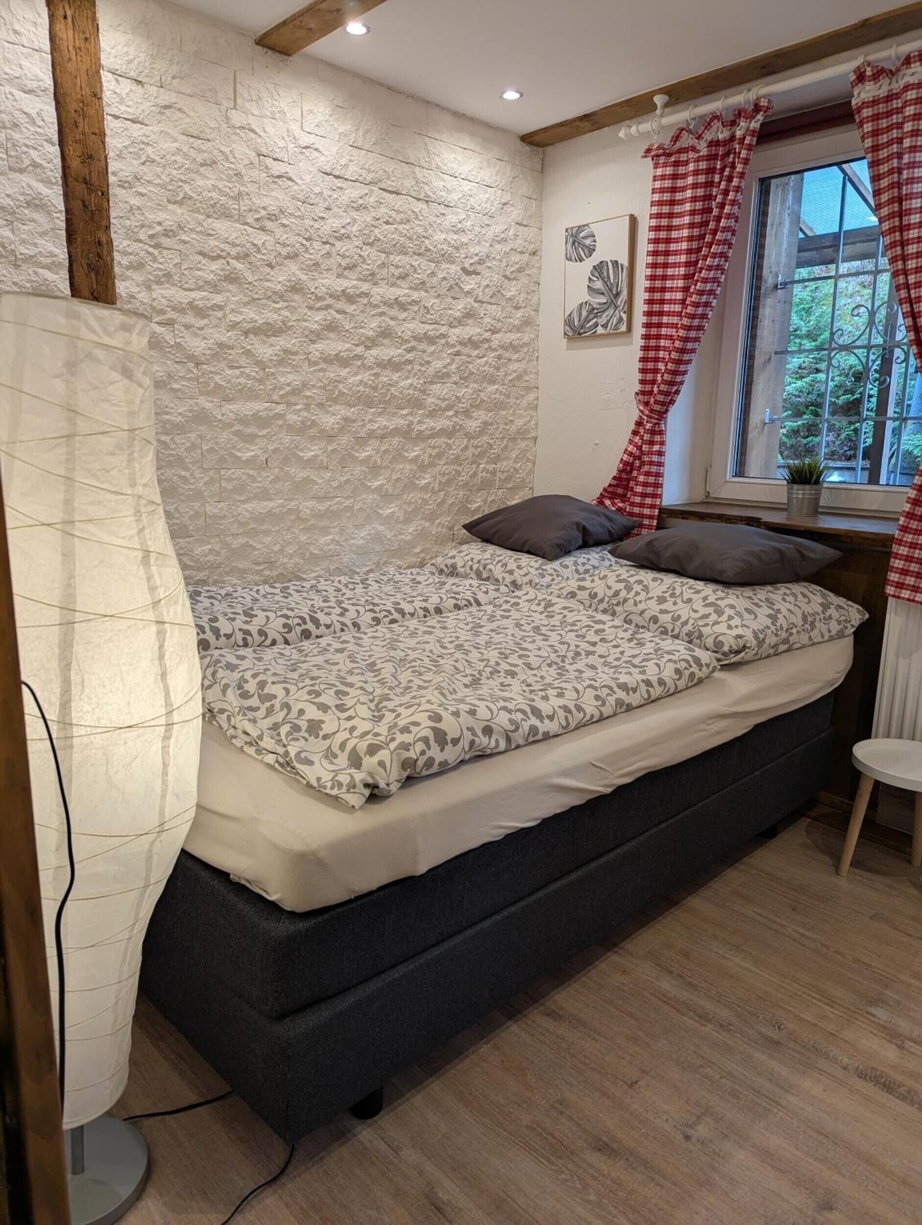 A bedroom with a bed, a window with curtains, a bedside table, and a wall with a textured pattern.