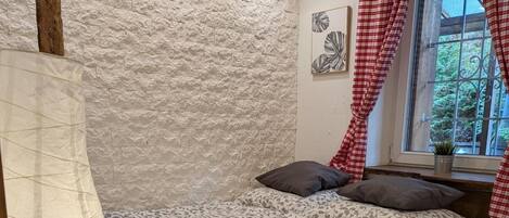A bedroom with a bed, a window with curtains, a bedside table, and a wall with a textured pattern.