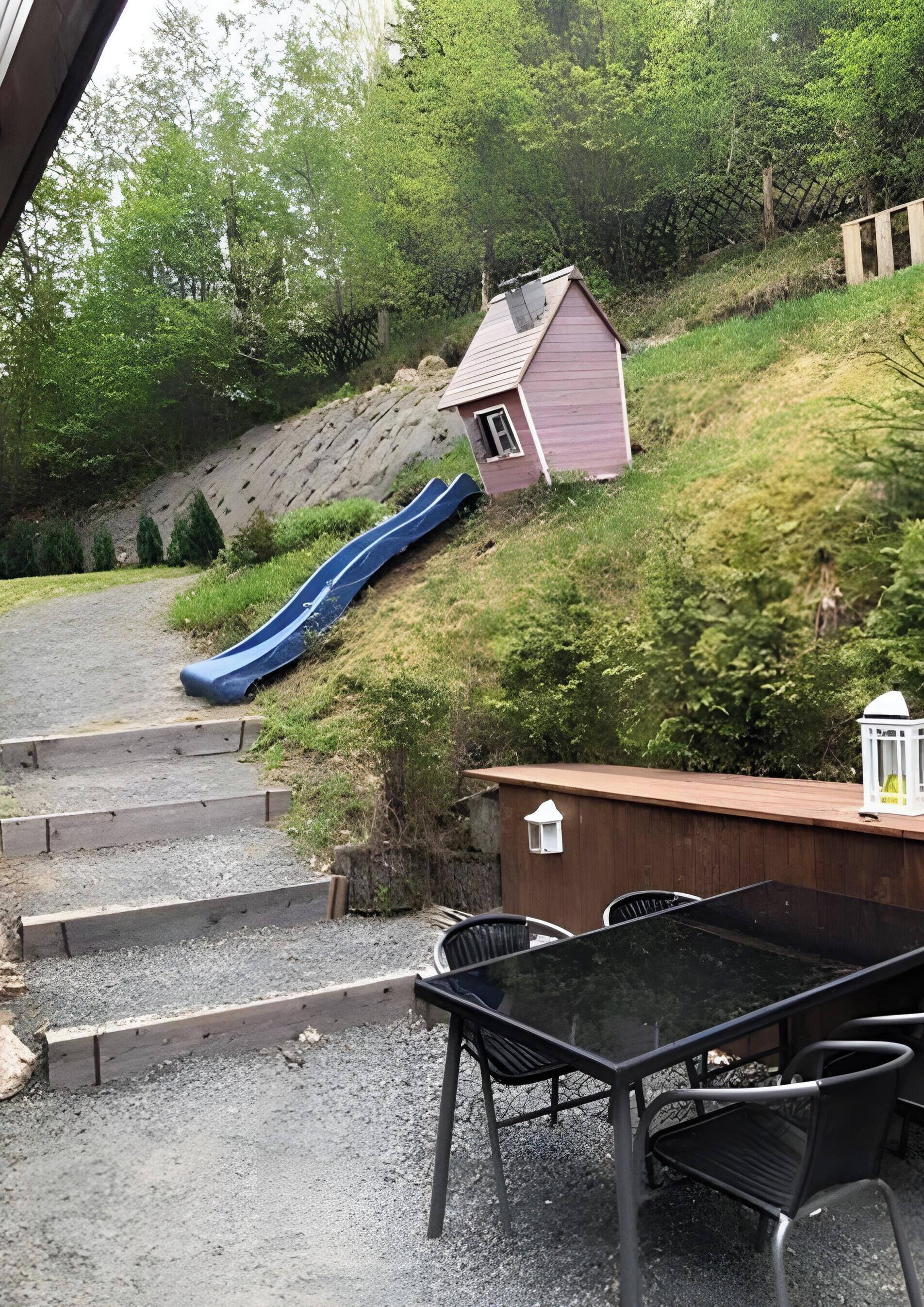 Eine Terrasse mit Tisch und Stühlen, eine kleine Gartenhütte, eine Rutsche und ein Holzdeck.