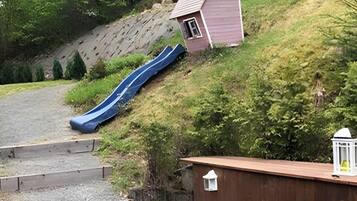 Eine Terrasse mit Tisch und Stühlen, eine kleine Gartenhütte, eine Rutsche und ein Holzdeck.