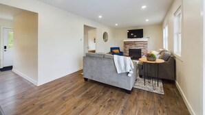 Ein geräumiger Wohnbereich mit grauem Sofa, einem kleinen runden Tisch und einem Kamin.
