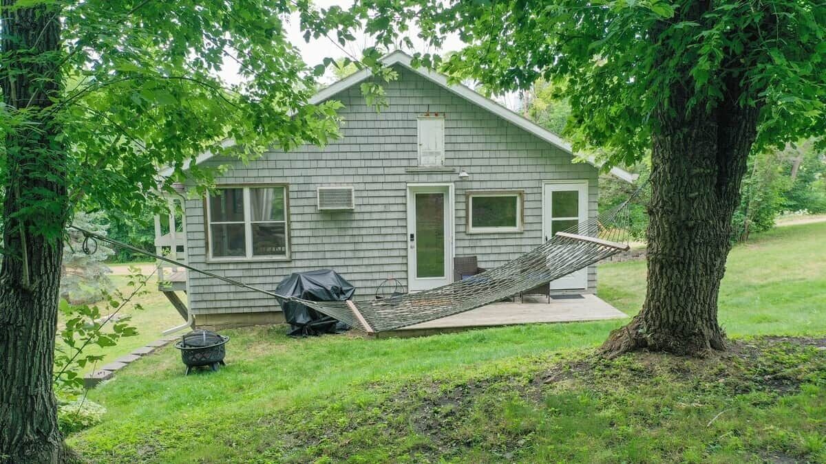 Une petite maison avec une véranda, un hamac et un barbecue.