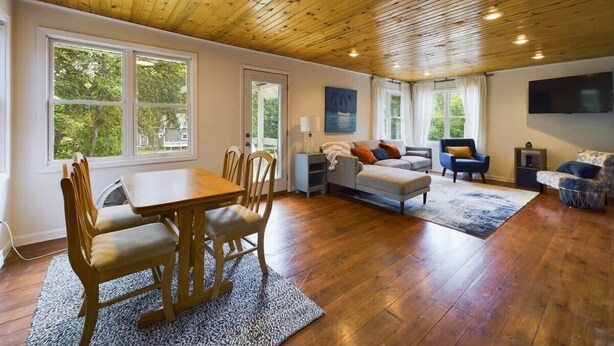 A spacious living room with a wooden ceiling, a dining area with a wooden table and chairs, a sofa, and a television mounted on the wall. - Cabin with private dock/beach access to Lake Minnewaska (Glenwood)