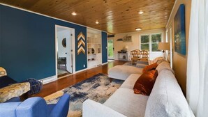 A spacious living room with a wooden ceiling, a large sofa set, and a built-in shelving unit. - Cabin with private dock/beach access to Lake Minnewaska (Glenwood)