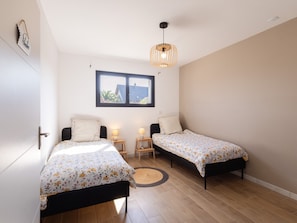 Un dormitorio con dos camas individuales, una ventana, una lámpara colgante y una puerta.