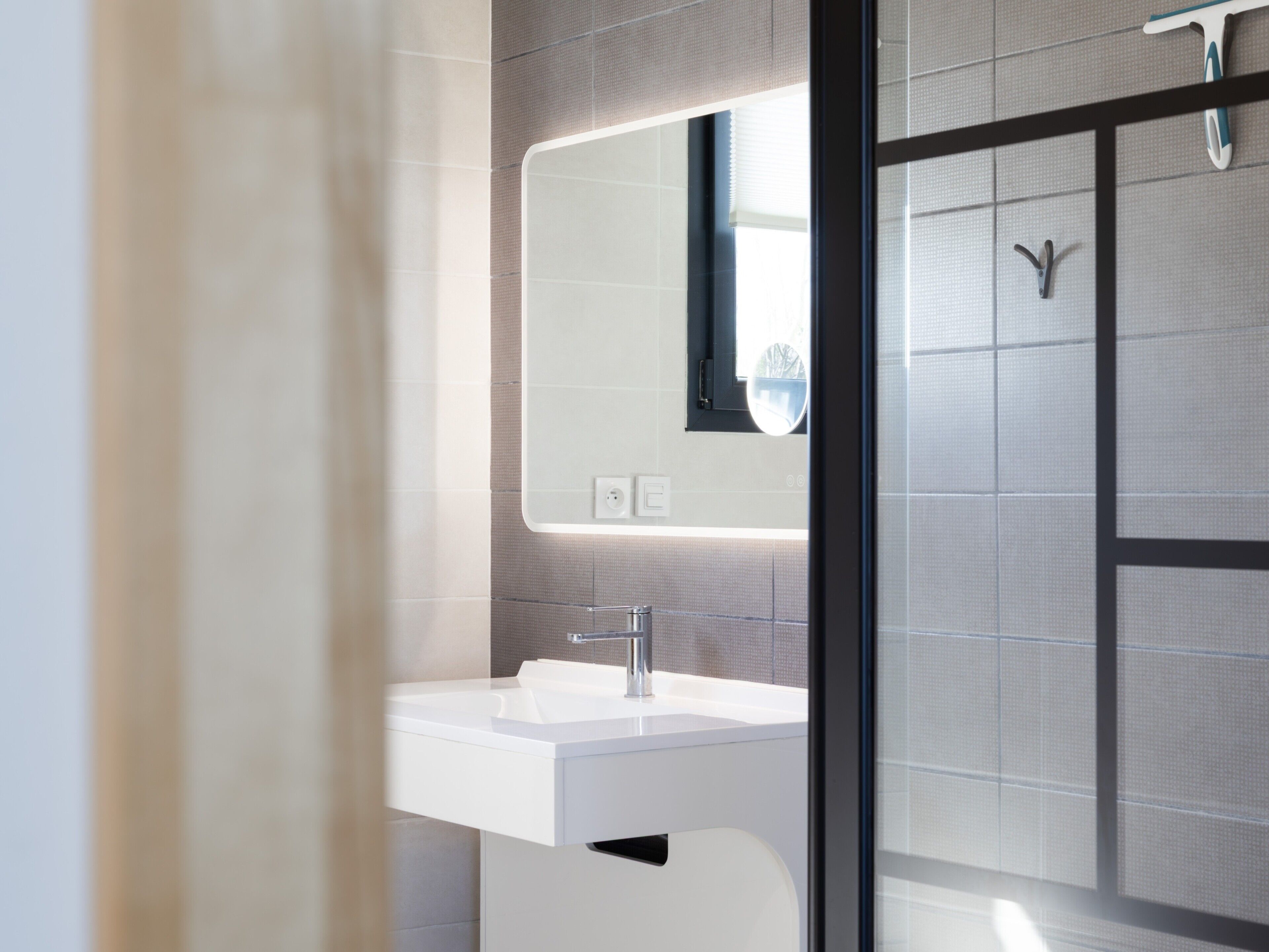 A modern bathroom with a white sink, a mirror, and a shower area.