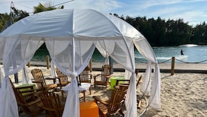 A beach cabana with a white canopy, wooden chairs, and a small orange table. - Bernsteinsee Hotel and Ferien-single Room (Sassenburg)