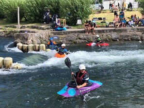 Ein Kajakfahrer bewegt sich einen Fluss hinauf, während eine Gruppe von Menschen vom Ufer aus zuschaut.