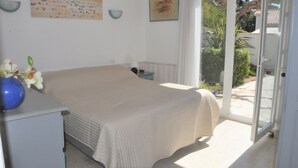 Een slaapkamer met een bed, nachtkastje, lamp en een vaas met bloemen.