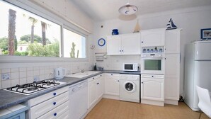 Een keuken met witte kasten, een gasfornuis, een wasmachine en een magnetron.
