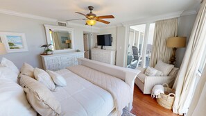 Ein Schlafzimmer mit Bett, Schreibtisch, Stuhl, Kommode, Fernseher und Deckenventilator.