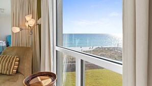 Ett rum med ett stort fönster med utsikt över en strand, en soffa med en randig kudde och en golvlampa.