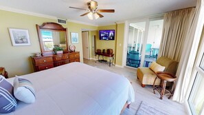A hotel room with a large bed, a dresser, a television, a balcony with chairs, and a ceiling fan. - 1043 Shoreline Towers Beachfront Condo Free Beach Setup (Destin)