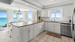 Een moderne keuken met witte kasten, een roestvrijstalen koelkast en een groot raam met uitzicht op de oceaan.