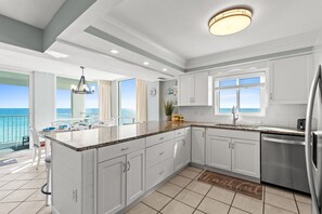 Eine moderne Küche mit weißen Schränken, einem Edelstahl-Kühlschrank und einem großen Fenster mit Blick auf den Ozean.
