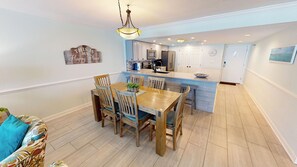 Un coin repas avec une table et des chaises en bois, une cuisine avec des meubles blancs et un mur d’accent bleu clair.