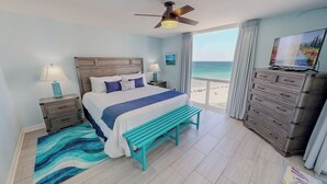 A hotel room with a bed, a bench, a dresser, a TV, a ceiling fan, and a view of the beach. - Beachfront 1072 w/Seasonal Beach Service (Destin)