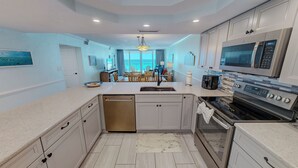 A modern kitchen with a dishwasher, oven, microwave, and a dining area with chairs and a table. - Beachfront 1072 w/Seasonal Beach Service (Destin)