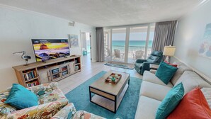 A living room with a television, bookshelves, a coffee table, and a sofa. - Beachfront 1072 w/Seasonal Beach Service (Destin)