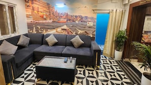 A reception area with a sofa, a coffee table, a mural of a cityscape, and a reception desk. - The Trishul Stay (Varanasi)
