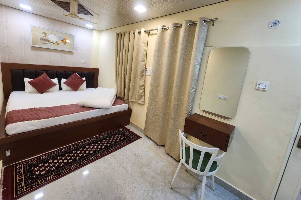 A bedroom with a bed, a chair, a dresser, a mirror, and a shower curtain.