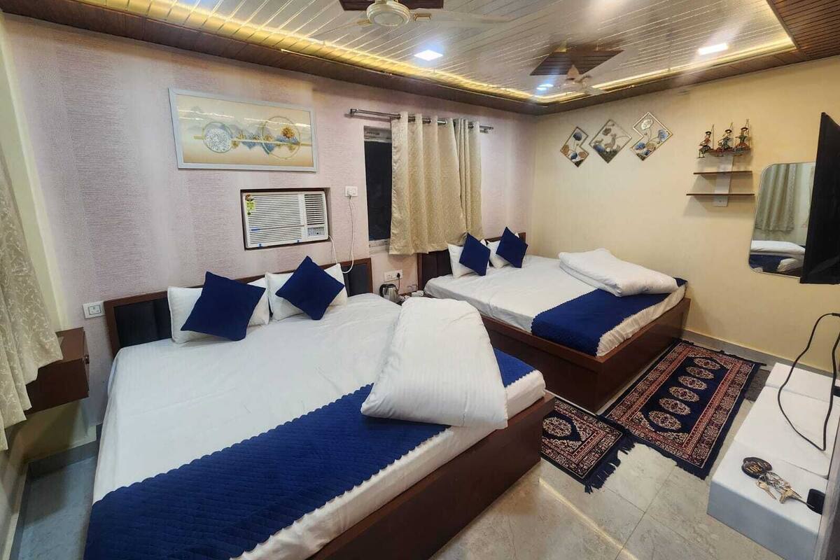 A hotel room with two beds, a ceiling fan, a window with curtains, a wall-mounted air conditioner, and a small rug.